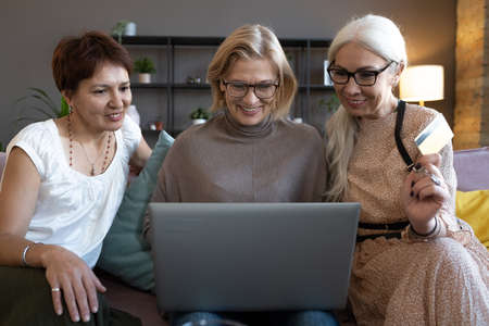 Happy senior women using computer together on the sofa, they doing shopping online and paying with credit cardの写真素材
