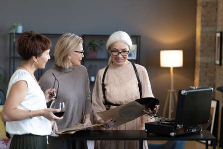 Group of happy mature friends drinking wine and listening to music on an old player during their...