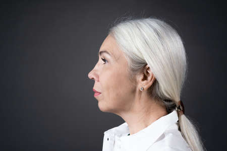 Side view of mature woman with long white hair looking away isolated on grey backgroundの写真素材