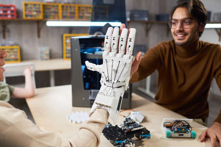 Student putting on the robotic arm on her hand and trying to control it, giving the high-five to her...