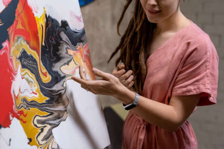 Close-up of young artist pointing at painted picture and talking about it during presentation in art...