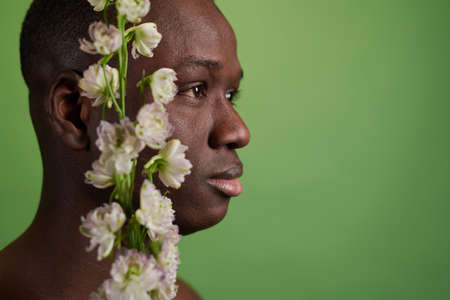 Side view of head of black man with white flowers looking forwards while standing in front of camera over green backgroundの写真素材