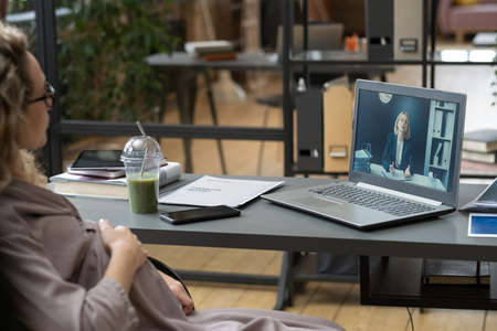 Young pregnant female office worker communicating to mature colleague about working points in video...