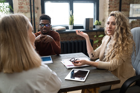 Young confident businesswoman in formalwear consulting female colleague while sitting by table...