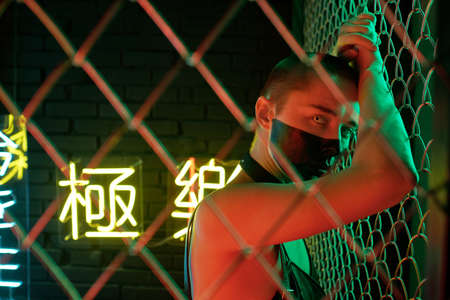 Young cyberpunk female looking at you while standing close to bars surrounding her from the rest of hacker hideoutsの写真素材