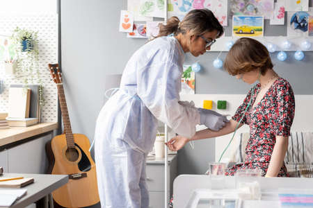 Young doctor in protective wear taking an analysis from the patient while she sitting on the bed at hospital wardの写真素材