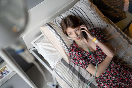 High angle view of sick girl having a conversation on mobile phone while lying on bed at hospital wardの写真素材