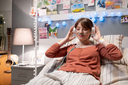 Sick woman in wireless headphones lying on the bed and enjoying the music during musical therapy while being treated at hospitalの写真素材