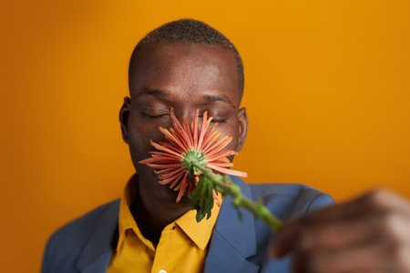 Close-up of African young man in suit smelling the flower and enjoying the smell of it against the...