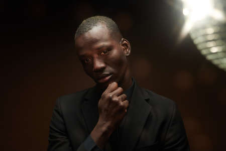 Portrait of African handsome man in elegant black suit looking at camera standing at nightclub with...