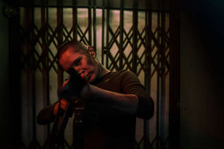 Waist up portrait of tough woman holding gun and looking at camera while standing in dark room ready...