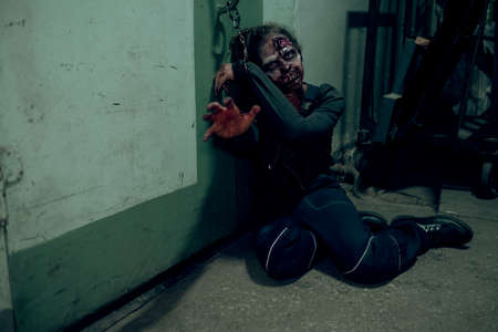 Full length shot of female zombie chained to wall in dark room and reaching to camera, copy space