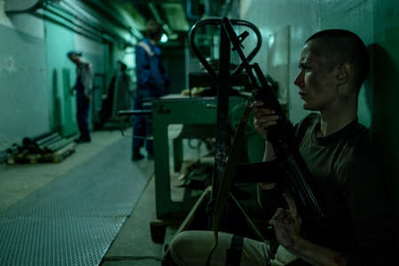 Side view portrait of female soldier holding gun while waiting in hideout for group of zombies in...