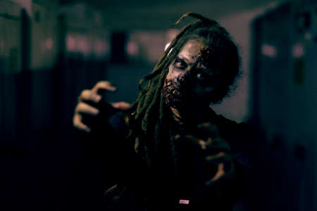 Front view shot of creepy female zombie looking at camera and reaching out in dark room
