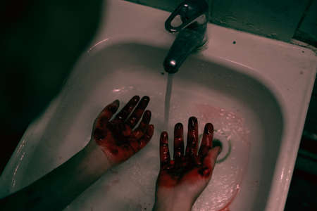 Top down view at tough woman washing bloody hands in shabby rusted sink, copy spaceの写真素材