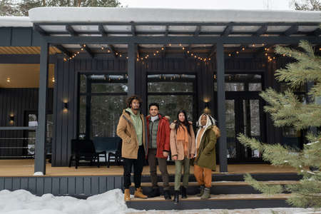 Portrait of group of young friends in warm clothing standing near the mansion and looking at camera, they spending weekends outdoorsの写真素材