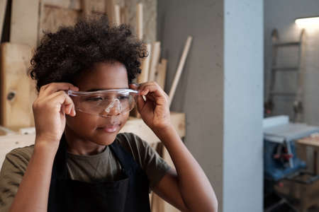 Portrait of cute African-American boy wearing protective glasses while helping father in workshop, copy spaceの写真素材
