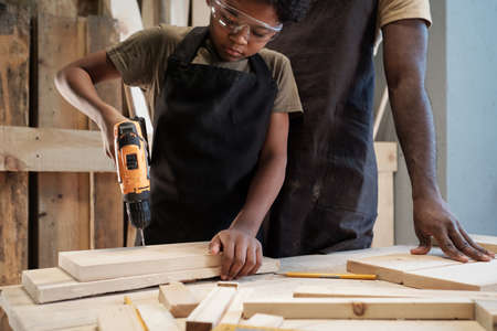 Cropped portrait of cute African-American boy building birdhouse in workshop with dadの写真素材