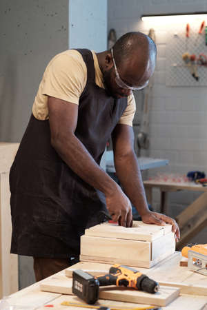 Vertical portrait of African-American mature carpenter building wooden furniture in workshopの写真素材