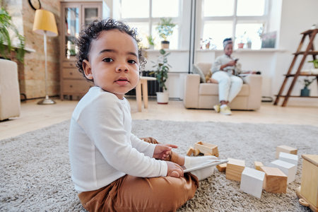 Portrait of serious cute African-American boy sitting on floor with wooden toys and holding tabletの写真素材