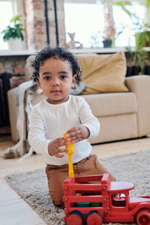Portrait of content little Mixed race boy with curly hair sitting on carpet and using screwdriver while repairing toy carの写真素材