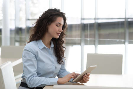 Pretty brunette female manager in formalwear touching screen of tablet while analyzing online data...