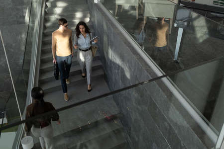 Two young employees of modern high tech company in formalwear moving downstairs while discussing...