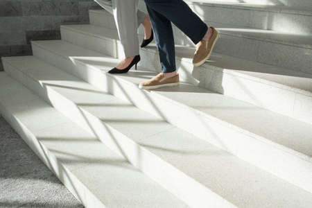 Legs of young contemporary male and female employees in formalwear moving down white marble...