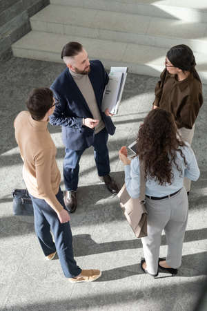 Young coworkers in formalwear standing inside large office center and having discussion of working...