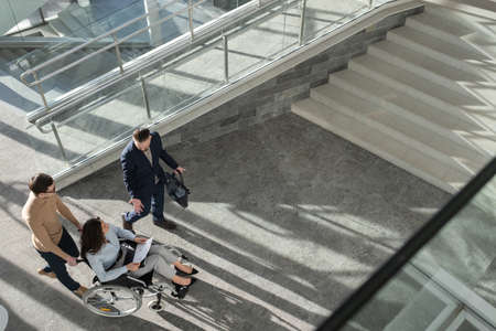 Above angle of confident ceo explaining business strategy to female colleague or partner with disability while moving along office centerの写真素材