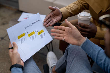 Hands of two contemporary intercultural businessmen discussing paper with evaluation data and...