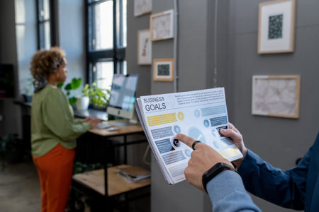 Hand of young businessman pointing at paper with business goals while discussing it with colleague...