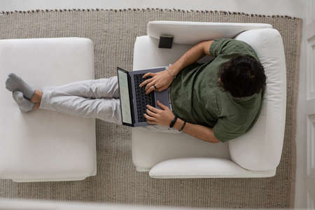 Overview of young male employee typing on laptop keyboard while looking through graphic data and...