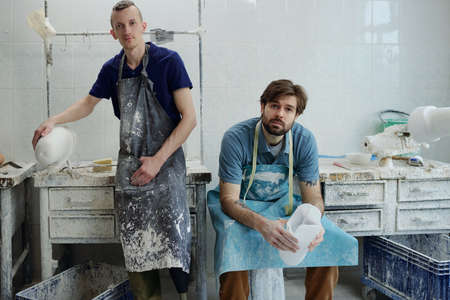 Young male staff of contemporary prosthetic factory in aprons looking at camera while making plaster...