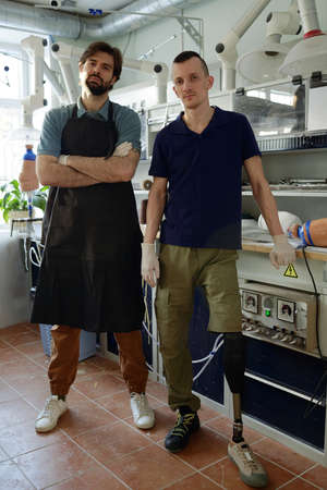 Young staff of modern prosthetic factory standing by workplace with workpieces of artificial limbs...