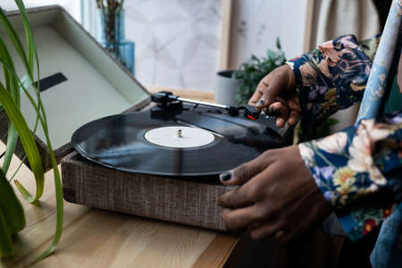 Hands of young black man with nail polish putting vinyl record on needle player standing on wooden windowsill before listening retro musicの写真素材