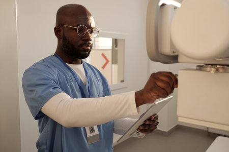 Young serious radiologist switching on x-ray equipment before examination of patients while standing in medical officeの写真素材