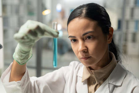 Contemporary scientist looking at flask with blue liquid substance during scientific experiment in...