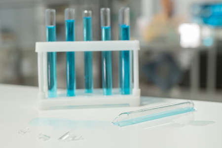 Shattered glass of broken test tube on desk against group of flasks with blue liquid in modern clinic or scientific laboratoryの写真素材