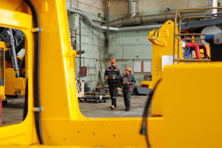 Two workers of large industrial plant moving along warehouse or workshop and consulting about...
