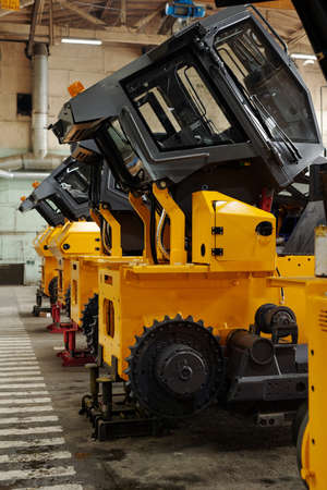 Several huge construction machines of yellow color standing in row on concrete floor of basement,...