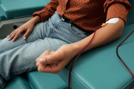 Close-up of young female donor in casual clothes giving her blood through hemotransfusion procedure in red zone of hospitalの写真素材