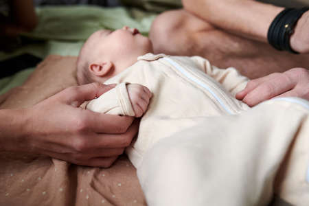 Adorable baby boy in white bodysuit lying on bed and sleeping between his parents touching him while enjoying leisure at homeの写真素材
