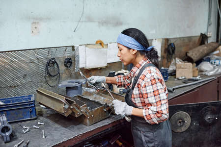 Young female worker of industrial plant choosing huge wrench for repair work while standing by...