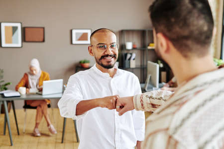 Happy young businessman in casualwear greeting his colleague with punch bump and looking at him...
