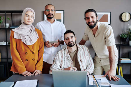 Four young successful Muslim office workers in casualwear looking at camera while preparing...