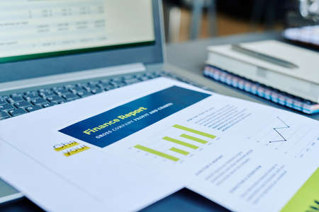Financial papers with statistics and profit information on keyboard of laptop with analyzed data on screen at workplace of accountantの写真素材