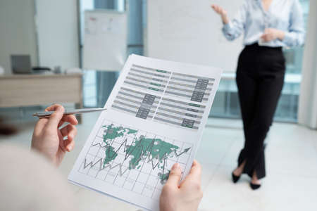 Hands of young female economist pointing at financial document with graphs while sitting in front of...