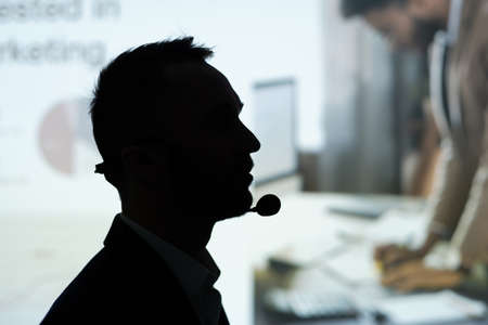 Profile outline of contemporary male broker or business coach speaking in microphone at seminar or conference during speechの写真素材