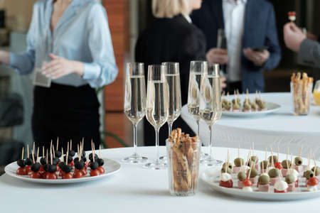Two plates with appetizing canape and group of champagne in flutes standing on served tables prepared for celebrationの写真素材